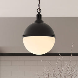 The Urban Ambiance ULB2000 Modern Farmhouse Pendant (17''H x 12''W, Matte Black, Apulon Collection) hangs from the ceiling above white tiled walls and a plant with delicate branches.