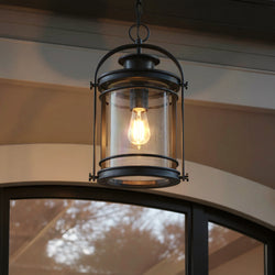 An Urban Ambiance UQL1011 Cannes Collection black silk finish pendant, 18"H x 10.5"W, hangs from the ceiling above a window, featuring mid-century modern style and exposed bulb design.