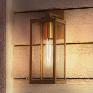 An UQL1341 Farmhouse Outdoor Wall Light, 17"H x 6"W, Antique Brass, Quincy Collection by Urban Ambiance providing unique lighting on a wooden wall.
