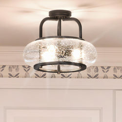The UQL3311 Utilitarian Ceiling Light from Urban Ambiance's Clearwater Collection features clear seedy glass shades and black metal accents on a white ceiling with patterned wallpaper, measuring 12"H x 16"W in a dark bronze finish, offering charm and style.