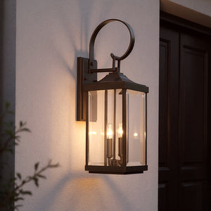 The UHP1193 Colonial Outdoor Wall Light by Urban Ambiance, 21-3/4" x 7", in Olde Bronze from the Calderdale Collection, is mounted on a light wall and casts a warm glow beside a dark-colored door.