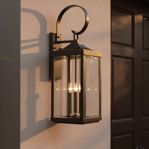 The Urban Ambiance UHP1194 Colonial Outdoor Wall Light (30-5/8" x 9-1/2", Olde Bronze, Calderdale Collection) is mounted on a beige wall by a wooden door, casting a warm glow at dusk.