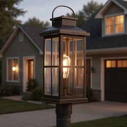 The UHP1293 Transitional Outdoor Post Light (20.25''H x 7''W) in Olde Bronze by Urban Ambiance stands in front of a house at dusk, casting a cozy glow with farmhouse style from the Anaheim Collection.