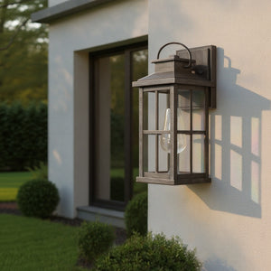 The Urban Ambiance UHP1295 Anaheim Collection Transitional Outdoor Wall Sconce, 14.25''H x 6''W in an aged pewter finish, is wall-mounted and shown on a home exterior beside a window with bushes and lawn.
