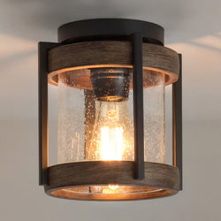 The Urban Ambiance UHP1352 Newark Collection Farmhouse Outdoor Ceiling Light features a cylindrical seeded glass shade, exposed bulb, wood accents, and a midnight black finish. Measures 8''H x 7.375''W.