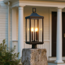 The Urban Ambiance UHP1400 Farmhouse Outdoor Post Light, 26.875''H x 9.5''W in a midnight black finish from the Calderdale Collection, is shown mounted on a stone pillar and illuminated in front of a house with white columns.