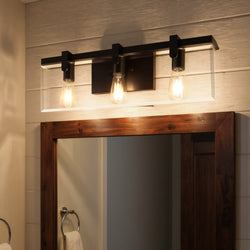 The Urban Ambiance UHP2450 Bristol Collection bath fixture, featuring an Olde Bronze finish and modern farmhouse style, is mounted above a wooden-framed mirror to add chic illumination to the bathroom.