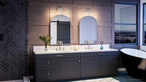 Modern bathroom featuring double sinks with gray cabinets, two arched mirrors, and the Urban Ambiance Parkes Collection UHP4222 Contemporary Bath Light (11.5′‘H x 22.125’’W) in brushed nickel finish with cylindrical glass shades. Stylish wall lights highlight a vase of flowers, while a freestanding black bathtub is positioned by the window offering a scenic view.