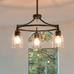 The UHP4272 Transitional Chandelier (12.25''H x 21''W, Midnight Black) from Urban Ambiance's Coronado Collection hangs illuminated, featuring clear glass shades with a window and trees in the background.
