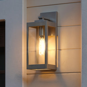 The Urban Ambiance UQL1360 Modern Farmhouse Outdoor Wall Light from the Quincy Collection, with a stainless steel finish (14.25"H x 5"W), is mounted on a light exterior wall and glows at dusk, elegantly displaying its visible bulb.