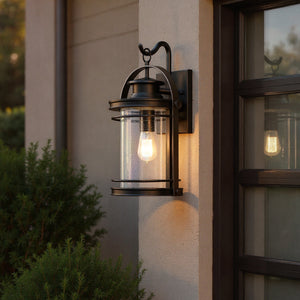 The Urban Ambiance UQL1432 Nautical Outdoor Wall Light from the Cannes Collection (18.25"H x 10.75"W, Black Silk Finish) glows warmly beside a garage door at dusk, surrounded by greenery.