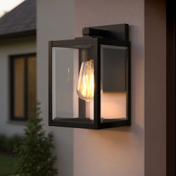 The Urban Ambiance UQL1890 Quincy Collection modern farmhouse outdoor wall sconce (10''H x 5.75''W), in a natural black finish, is mounted near a window and landscaping on this stylish house exterior.