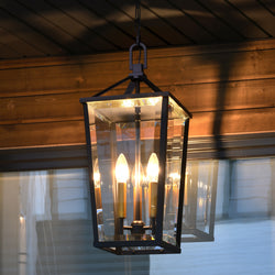 The Urban Ambiance UQL1960 Urban Loft Outdoor Pendant, 22"H x 9.5"W, in matte black from the Ulm Collection, features clear beveled glass and four candle-style bulbs for elegant porch lighting.