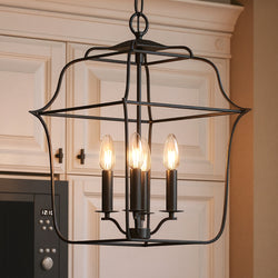 The UQL2321 Colonial Chandelier by Urban Ambiance, featuring a vintage black finish and four exposed bulbs, hangs in front of white kitchen cabinets, bringing elegant Savannah Collection style to the space.
