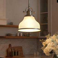 The Urban Ambiance UQL2336 Industrial Pendant Light in brushed nickel hangs in a kitchen with wooden shelves, a tiled backsplash, and a vase of white flowers on the counter.