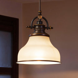 The Urban Ambiance UQL2338 Industrial Pendant Light from the Pasadena Collection features a Parisian Bronze finish and opal etched glass shade, creating a warm glow against a beige wall. Measures 9.5"H x 8"W.