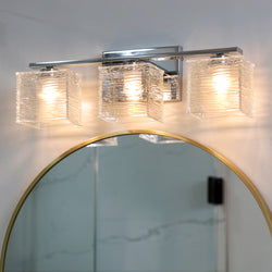The Urban Ambiance UQL2723 Modern Bathroom Light from the San Diego Collection features a polished chrome finish and sandblasted glass shades, mounted above a gold-framed round mirror to bring stylish, modern lighting to your bathroom.