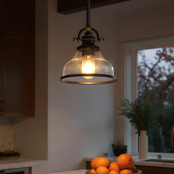 The Urban Ambiance UQL3660 Pasadena Collection traditional pendant (9.5''H x 8''W) in Parisian Bronze with opal etched glass hangs above a kitchen counter holding oranges, with a window and plants in the background.