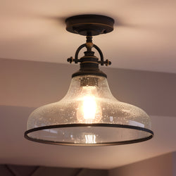 The Urban Ambiance UQL3668 ceiling light from the Pasadena Collection features a Parisian Bronze finish, clear speckled glass shade, and exposed bulb, blending industrial style for a warm, inviting glow.