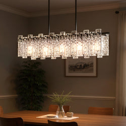 The Urban Ambiance UQL4630 Glam Chandelier from the Rockingham Collection in matte black, featuring rippled textured glass and exposed bulbs, hangs above a wooden dining table with artwork and curtains in the background.