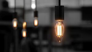 Close-up of an Urban Ambiance UBB2042 Luxury LED Bulb, 60W equivalent, vintage Edison style (B11 E12 candelabra base, 2700K), with similar bulbs softly blurred in the background.