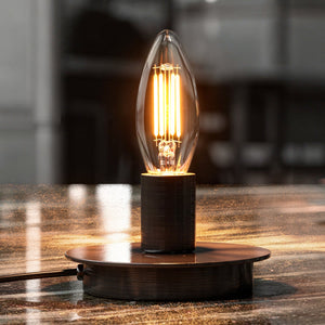 An Urban Ambiance UBB2042 Luxury LED B11 E12 vintage Edison bulb glows warmly on a round metal base, its light reflecting off an indoor surface.