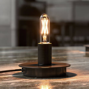 A black metal lamp with a Urban Ambiance UBB2133 Luxury LED Vintage Edison candelabra bulb (T6, E12 base, 3000K, 40W equivalent) sits on a reflective marble surface with a blurred background.