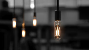 Four Urban Ambiance UBB2133 Luxury LED Bulbs, 40W Equivalent, Vintage Edison Style with E12 candelabra base and warm 3000K glow, stand out against a blurred dark background—three softly glowing, one sharply focused.