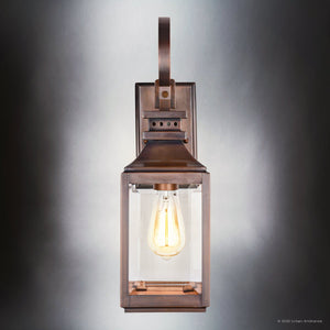 The UFS1000 Transitional Outdoor Wall Sconce by Urban Ambiance, part of the Calderdale Collection, features genuine copper with a dark-patina finish, a clear glass enclosure, and visible glowing bulb. Size: 15''H x 5.5''W.