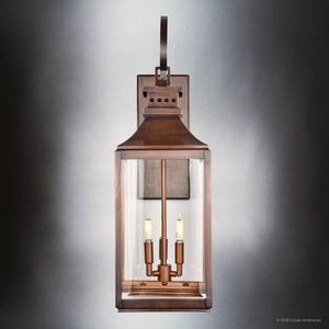 The UFS1002 Transitional Outdoor Wall Sconce from Urban Ambiance's Calderdale Collection features genuine copper with a dark-patina finish, beveled glass panels, and two visible bulbs, shown against a neutral gradient background.