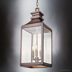 The Urban Ambiance UFS1004 Calderdale Collection pendant light, featuring genuine copper with a dark patina and beveled glass, hangs by a chain against a plain gray background. Measures 26.5''H x 9.5''W with four exposed bulbs.