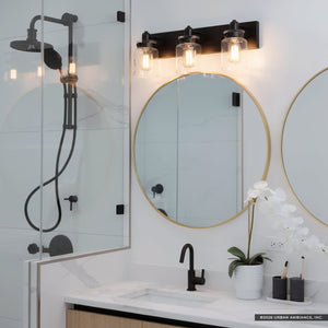 Modern bathroom with glass shower, black fixtures, round gold-framed mirror, and a white countertop, featuring the Urban Ambiance UHP2143 Modern Farmhouse Industrial Bath Fixture from the Bridgeport Collection in an Olde Bronze finish above the vanity, complemented by a white orchid in a pot.