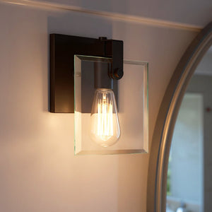 Certainly! Here’s a rewritten sentence using the provided product data: The Urban Ambiance UHP2454 Modern Farmhouse Bath/Wall Light from the Bristol Collection features an Olde Bronze finish and square beveled glass panel, mounted next to a large round mirror and softly illuminating the space with its exposed filament bulb.
