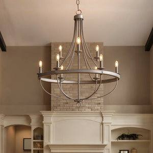 The Urban Ambiance UHP2902 XL Farmhouse Chandelier from the Adelaide Collection, featuring a galvanized steel finish, an open cage design, and eight exposed lightbulbs within its 40-1/2″ x 35″ round frame, hangs from the ceiling in a living room with beige walls and a brick fireplace.