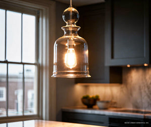 The UHP3043 Modern Farmhouse Pendant Light from Urban Ambiance’s Dundee Collection, featuring a hand-blown glass shade and a brushed nickel finish, hangs in a modern kitchen with a window and countertop visible in the background.