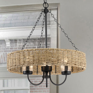 The UHP4781 Casual Indoor Chandelier from the Bexley Collection by Urban Ambiance, featuring weather-resistant rattan and a matte black metal frame with vintage-style bulbs, elegantly hangs in front of a window. Its dimensions are 21-1/2''H x 20