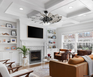 A modern living room showcases the Urban Ambiance UHP9482 Tuscan Indoor Ceiling Fan in matte black, white coffered ceiling, two leather chairs, a tan sofa, and a fireplace under a wall-mounted TV. Shelves with decor and a street-view window complete this elegant space.
