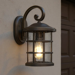 The Urban Ambiance UQL1043 Craftsman Outdoor Wall Light, 14.25"H x 8"W, Vienna Collection in Parisian Bronze with marine-grade construction is mounted on a beige stucco wall near a garage door, resembling a classic lantern-style sconce.
