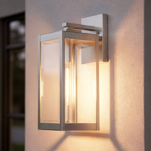 The Urban Ambiance UQL1361 Modern Farmhouse Outdoor Wall Light from the Quincy Collection features a 17-inch tall by 6-inch wide rectangular metal and glass frame in a stainless steel finish. Designed for mounting on stucco exterior walls, this durable fixture blends contemporary style with farmhouse charm to provide warm, inviting illumination at your entryway.