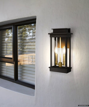 The Urban Ambiance UQL1820 New Traditional Outdoor Wall Sconce from the Selby Collection, featuring a matte black finish and marine-grade construction, is mounted on a white textured wall beside a window with horizontal blinds.
