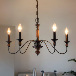 The Urban Ambiance UQL2350 Americana Chandelier from the Raleigh Collection, featuring five candle-style bulbs and a rustic bronze finish, hangs from the ceiling in a softly lit room with neutral-colored walls and warm wood-tone accents, bringing an inviting Americana style to the space.