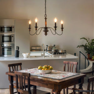 A kitchen featuring a wooden dining table, a bowl of apples, a white countertop, stainless steel appliances, wood-tone accents, a potted plant, and the Urban Ambiance UQL2350 Americana Chandelier from the Raleigh Collection in rustic bronze finish (14.25″H x 24″W) hanging above.