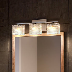 The UQL2722 Modern Bathroom Light by Urban Ambiance, featuring a brushed nickel finish and wavy glass shades, is mounted above a rectangular mirror with a wooden frame on a dark tiled wall, creating the perfect modern bath fixture.