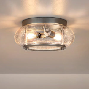 The UQL3290 Utilitarian Ceiling Light from Urban Ambiance’s Clearwater Collection features a brushed nickel finish and a 12″ wide clear seeded glass shade with two visible bulbs, providing modern farmhouse style illumination against any white ceiling.