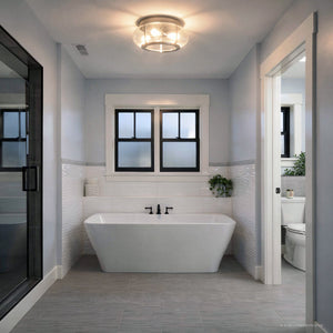 Modern bathroom with freestanding bathtub, frosted window, black fixtures, gray tile floor, glass shower door to the left, and a small plant on the ledge behind the tub. The space is beautifully illuminated by the Urban Ambiance UQL3300 Utilitarian Ceiling Light from the Clearwater Collection (7″H x 16″W) in a brushed nickel finish, which features seeded glass for a touch of contemporary charm.
