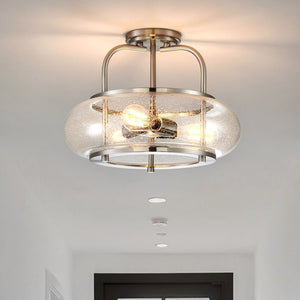 Urban Ambiance UQL3310 Utilitarian Ceiling Light from the Clearwater Collection, featuring a brushed nickel finish, two exposed bulbs, and a clear seeded glass shade, is mounted on a white hallway ceiling.