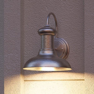 An UHP1022 Industrial Chic Outdoor Wall Light with an Aged Nickel Finish from the Palermo Collection by Urban Ambiance providing luxury lighting on a brown wall.