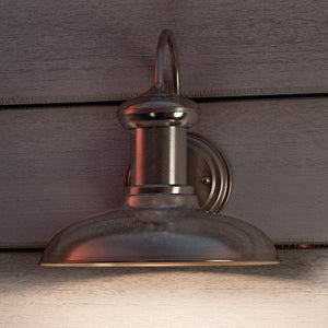 Industrial design elements shine in the Urban Ambiance UHP1025 Luxe Industrial Chic Outdoor Wall Light from the Palermo Collection, featuring an aged nickel finish and a domed shade, measuring 10.75″ high by 10″ wide, beautifully mounted on horizontal wooden siding and casting a soft glow below.