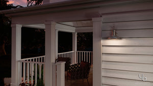 A covered porch with a white railing, two chairs, and a table is illuminated by the Urban Ambiance UHP1025 Luxe Industrial Chic Outdoor Wall Light from the Palermo Collection (10.75″H x 10″W) in an aged nickel finish, adding a touch of industrial design at dusk.