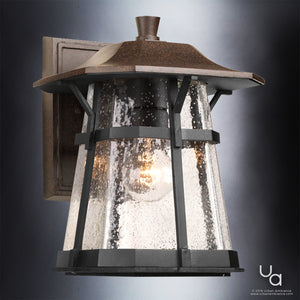 The Urban Ambiance UHP1071 Rustic Outdoor Wall Light from the Gold Coast Collection features a metal and glass design with an 11.25-inch height, 8.5-inch width, a square backplate, sloped top, and a visible bulb inside clear textured glass panels in a coffee bronze finish—bringing rustic coastal charm to any exterior.